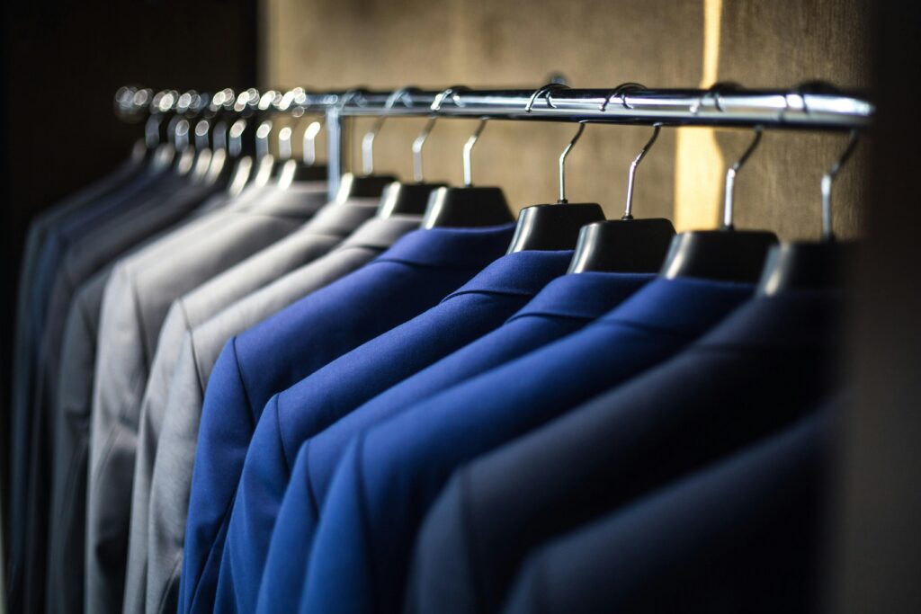 Tailored men's custom suits in blue and gray hanging on a rack.